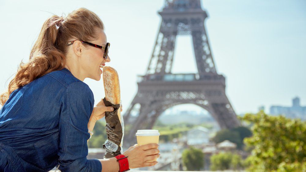 Kobieta jedząca bagietkę przed Wieżą Eiffla