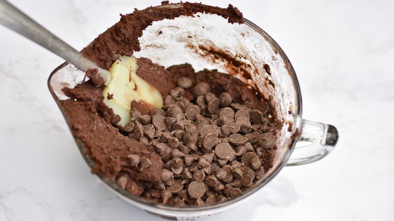 Łopatka w przezroczystym pojemniku wypełnionym ciastem czekoladowym i kawałkami czekolady