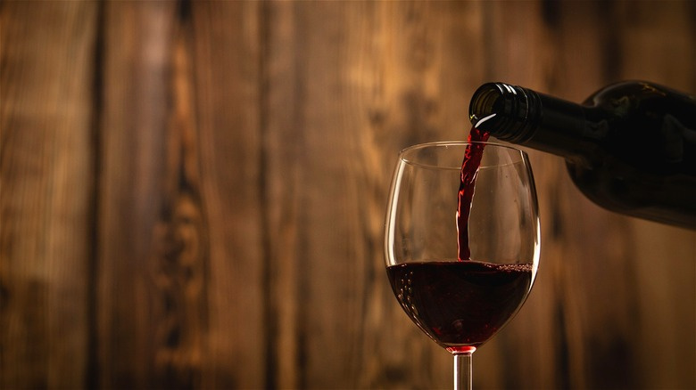   Czerwone wino nalewane do kieliszka, drewno z tyłu